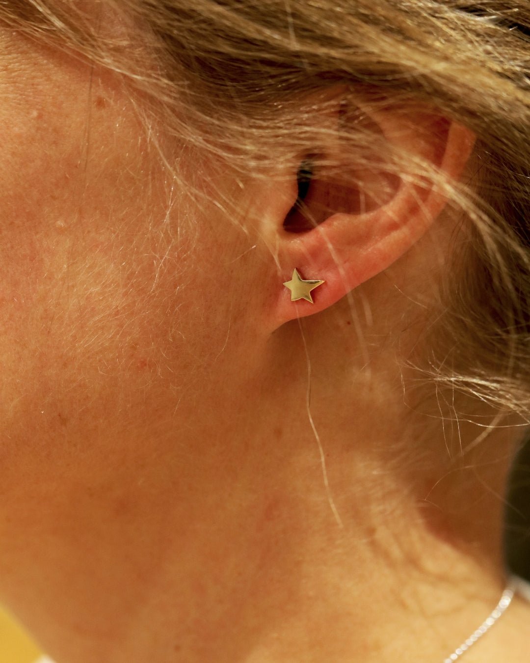Small 18K gold star stud earring on the earlobe