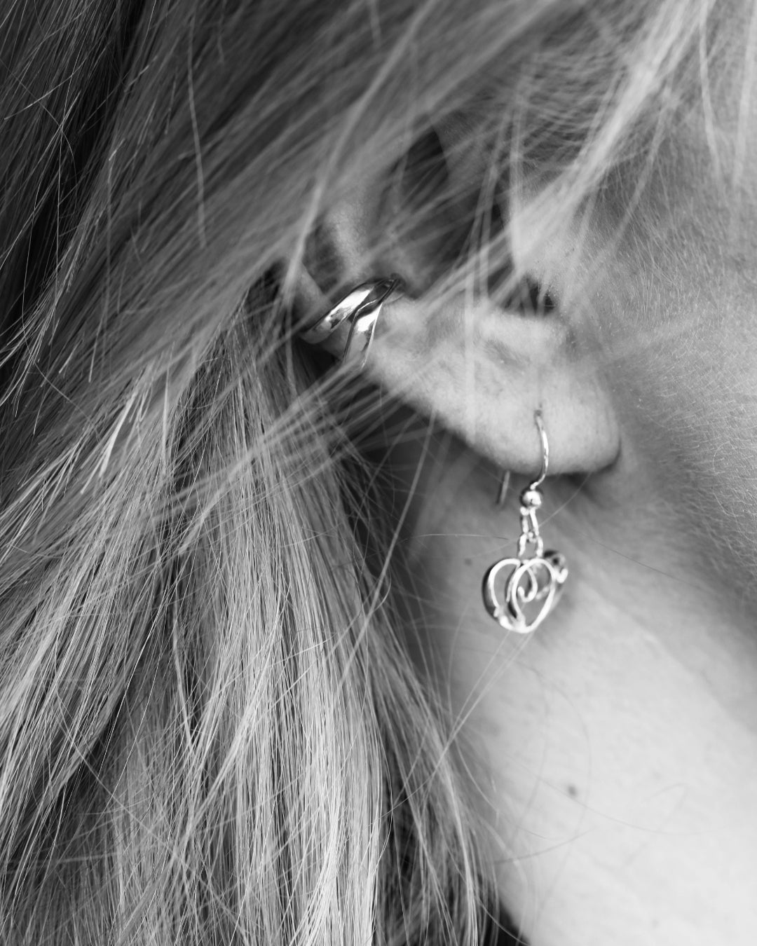 Side view of ear with a STORMSKÄRS MAJA ear cuff and a dangling heart-shaped hoop earring