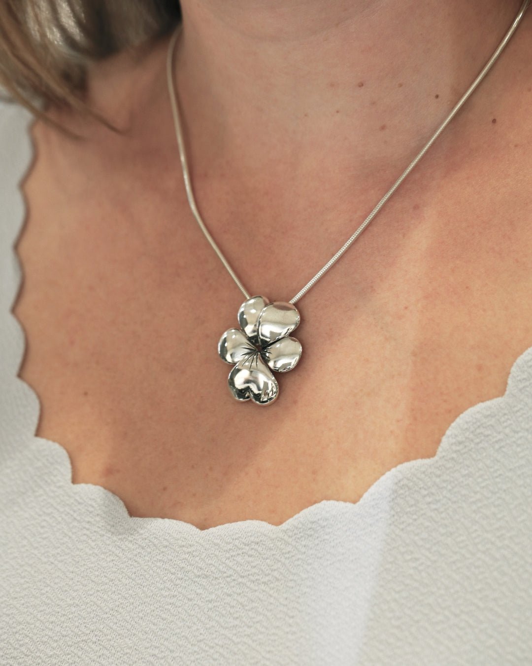 VIOL halsband med blomformigt hänge i silver visas mot halsen i närbild