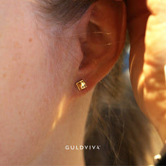 Close-up of a square 18K gold stud earring worn on the earlobe.