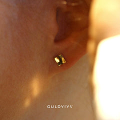 Close-up of a square 18K gold stud earring worn on the earlobe in warm light.