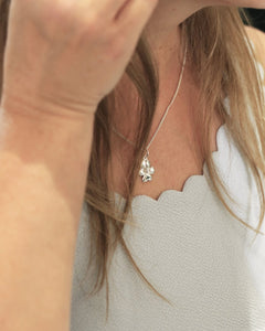 Close-up of a silver VIOL S flower pendant necklace worn around the neck