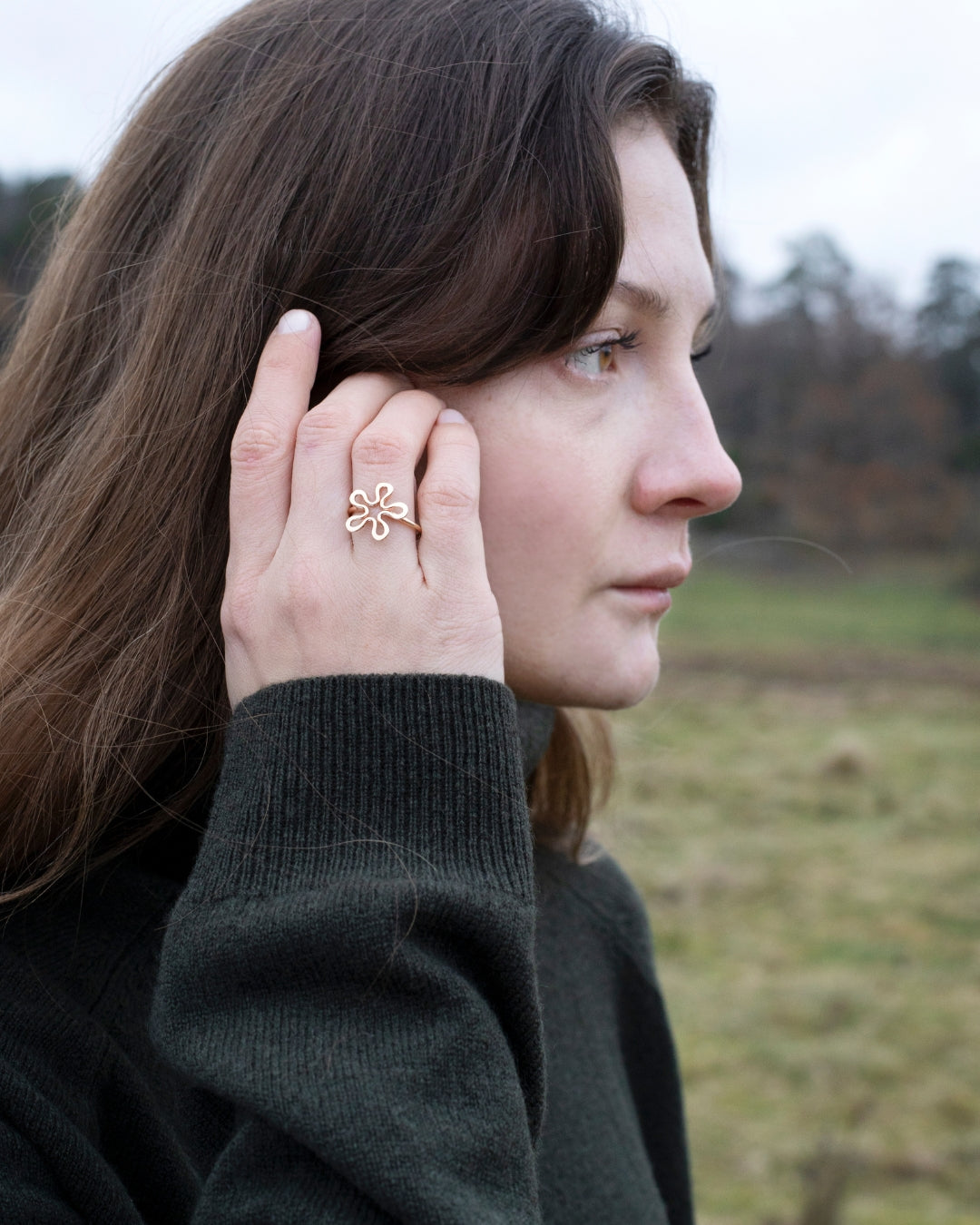 Model wearing BLOMMAN 18K rose gold ring with flower motif on finger outdoors.