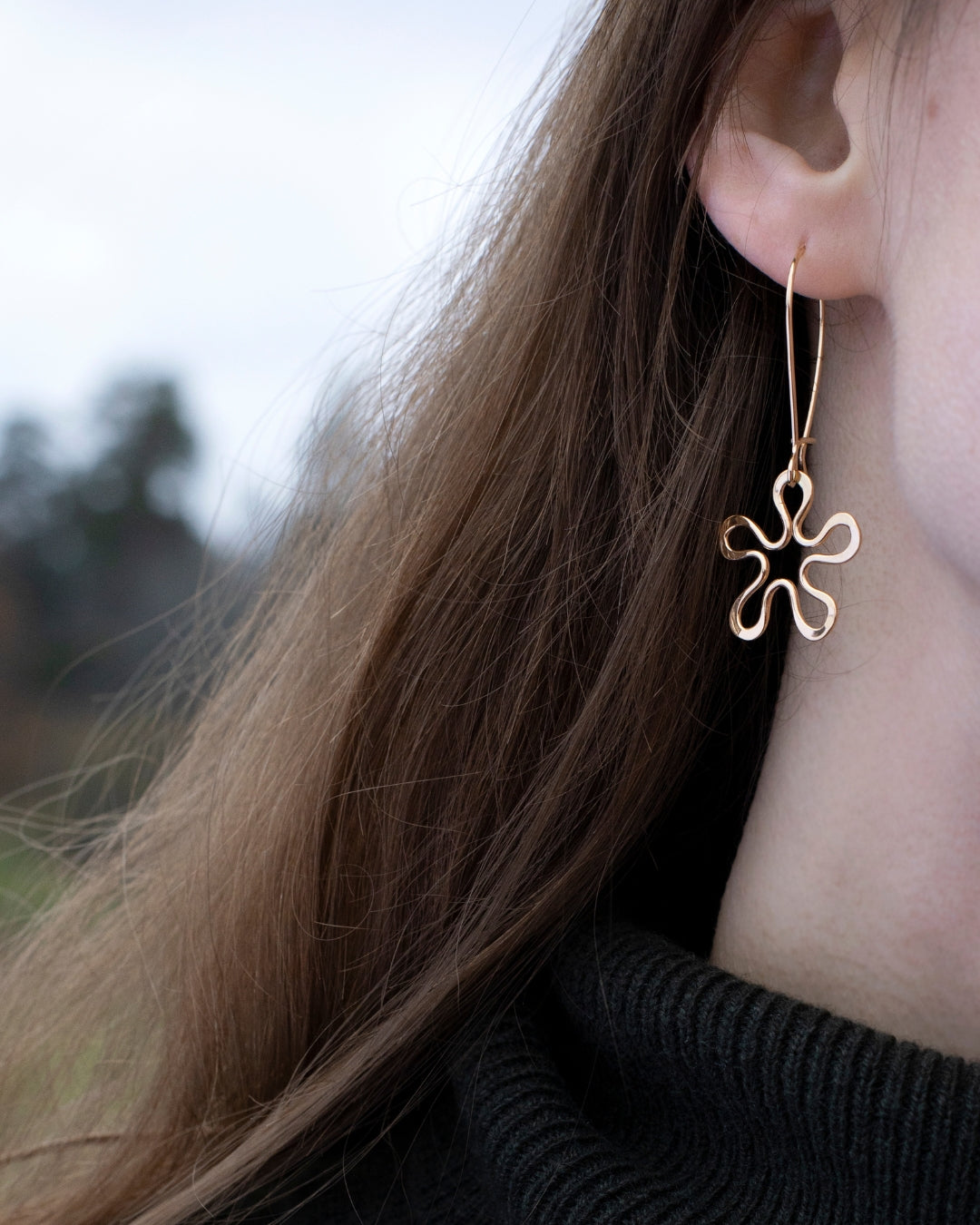 Närbild av BLOMMAN 18K Elegant örhänge på krok i guld fäst i öra med blomformad design