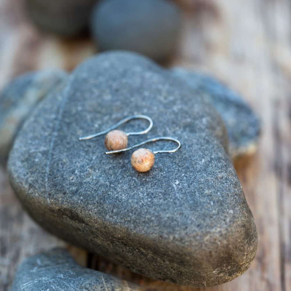 Två STRAND örhängen på krok med ljusa strandstenar ligger på en sten