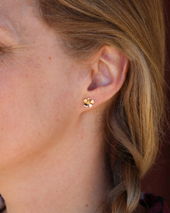 Close-up of a woman wearing 18K gold flower stud earrings on the earlobe