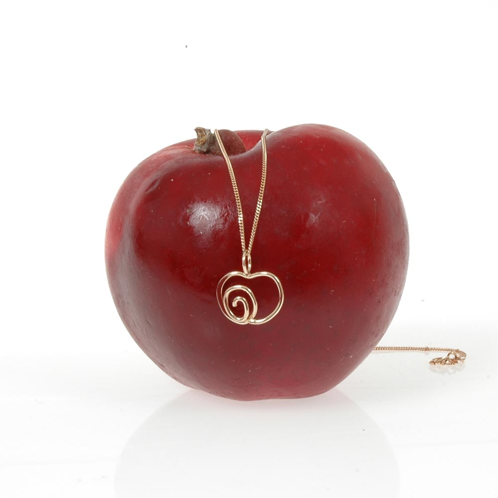 Gold spiral heart pendant resting on a red apple with the chain nearby