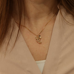 Close up of a gold flower cluster pendant on a thin chain at the collarbone