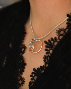 Närbild av Argentum Delicata halsband med spiraläppelsmycke i silver mot modellens svarta spetsklänning