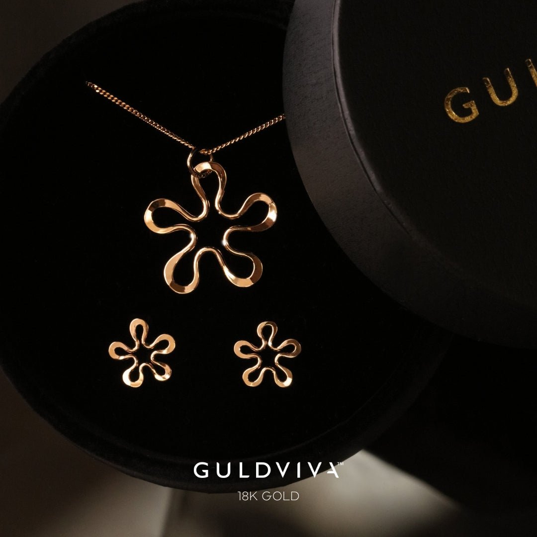 18K gold blomman flower pendant with matching stud earrings on a black display