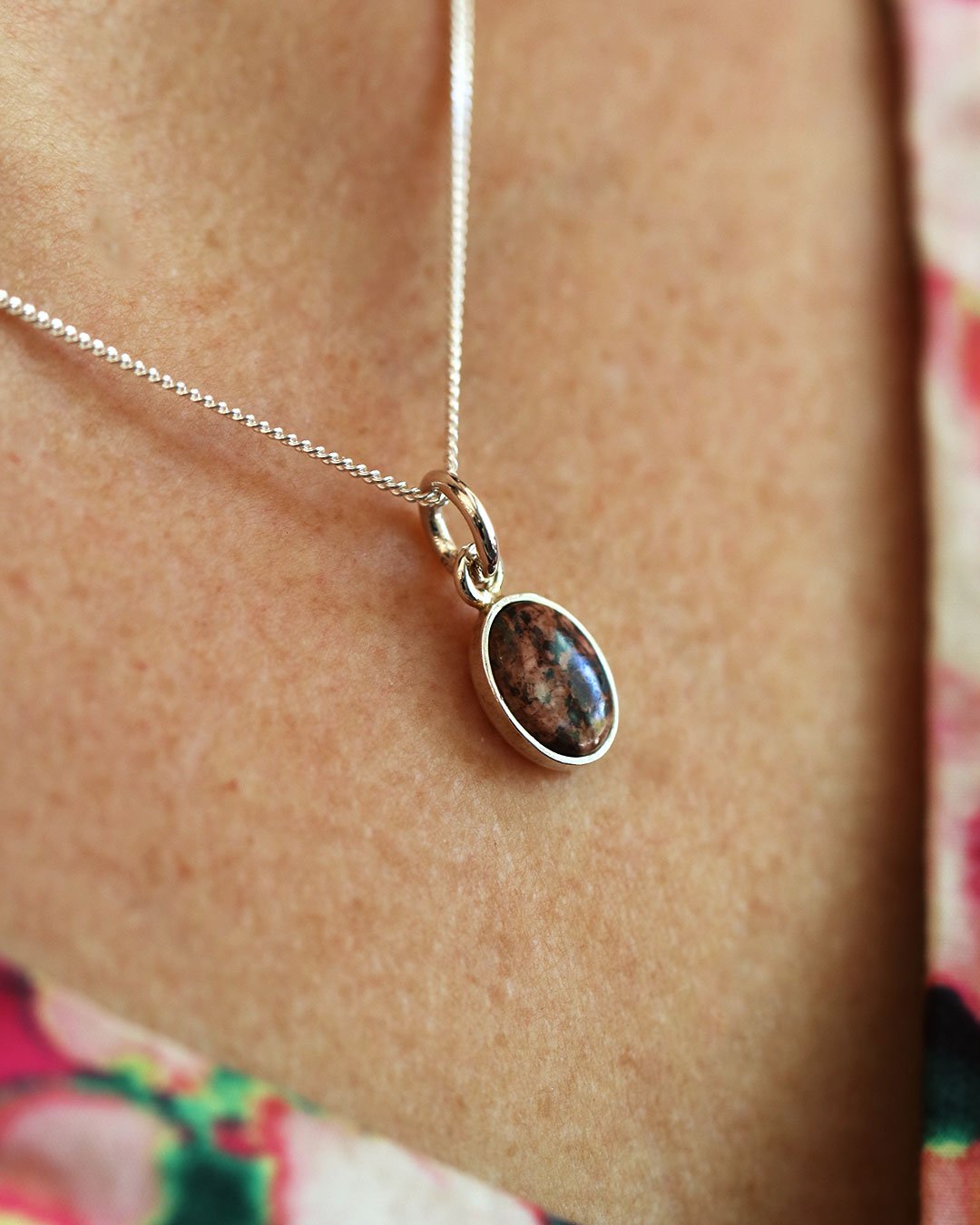 Oval red granite pendant in a silver bezel on a silver chain worn on the neck.