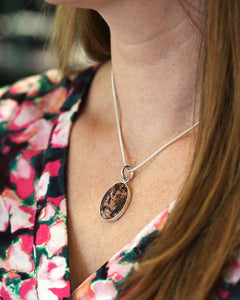 Silver chain with oval granite pendant worn at the neck by a person in a floral blouse