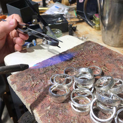 Jeweler's workshop with pliers shaping a silver ring over a textured work surface and several finished rings