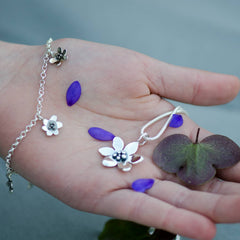 Handen visar ett silver armband med små blomformade berlocker och blå blåsippor runt
