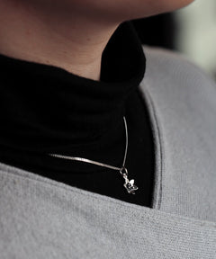 BLÅSIPPA XS halsband i 925 sterling silver med en liten blomma som hänger framför en svart polotröja