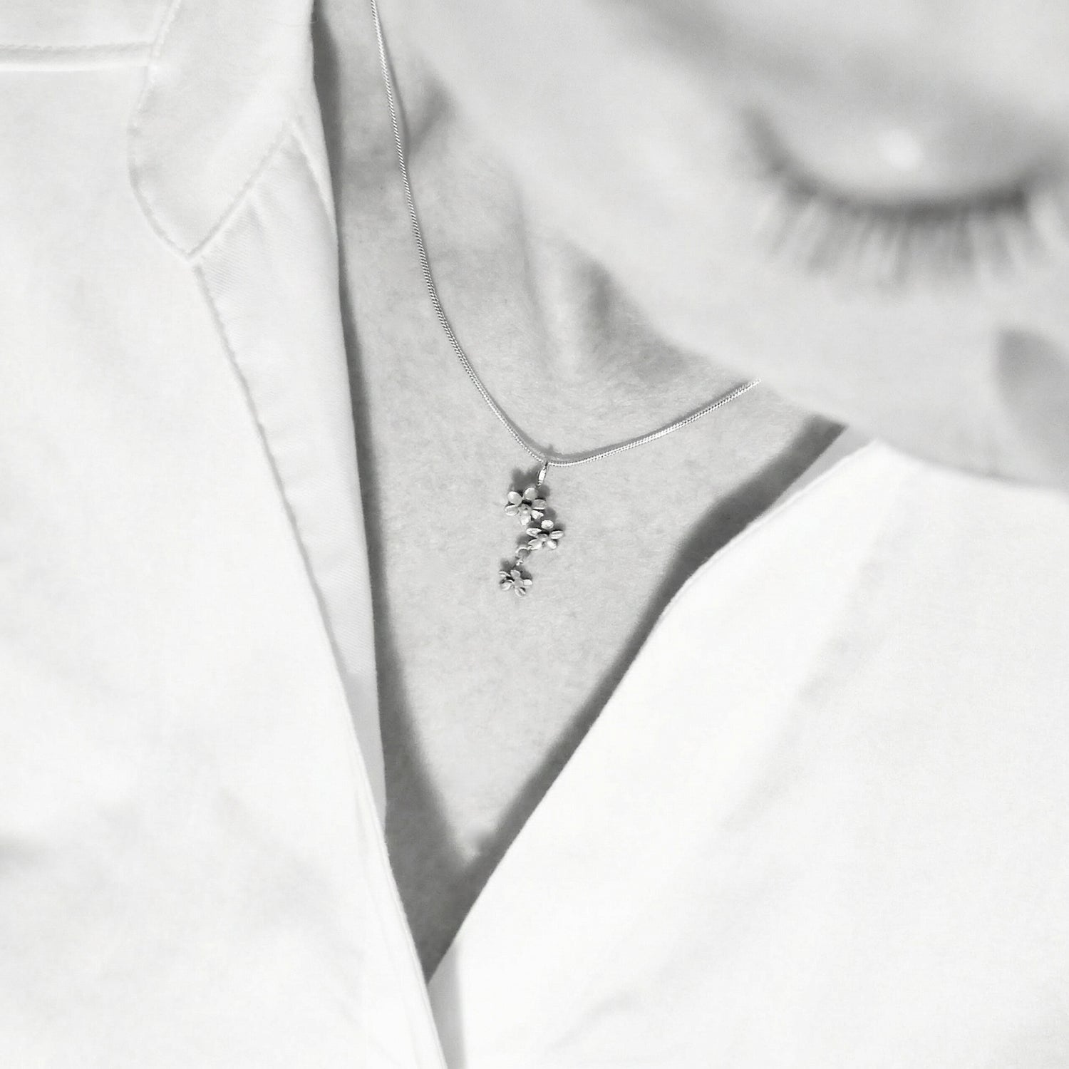 Close up of a silver flower pendant necklace worn on a model against a light top.