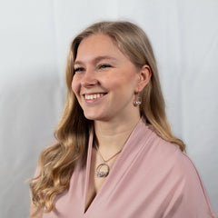 Kvinna bär GLORY L halsband med rund silverram och vågmotiv samt matchande örhängen