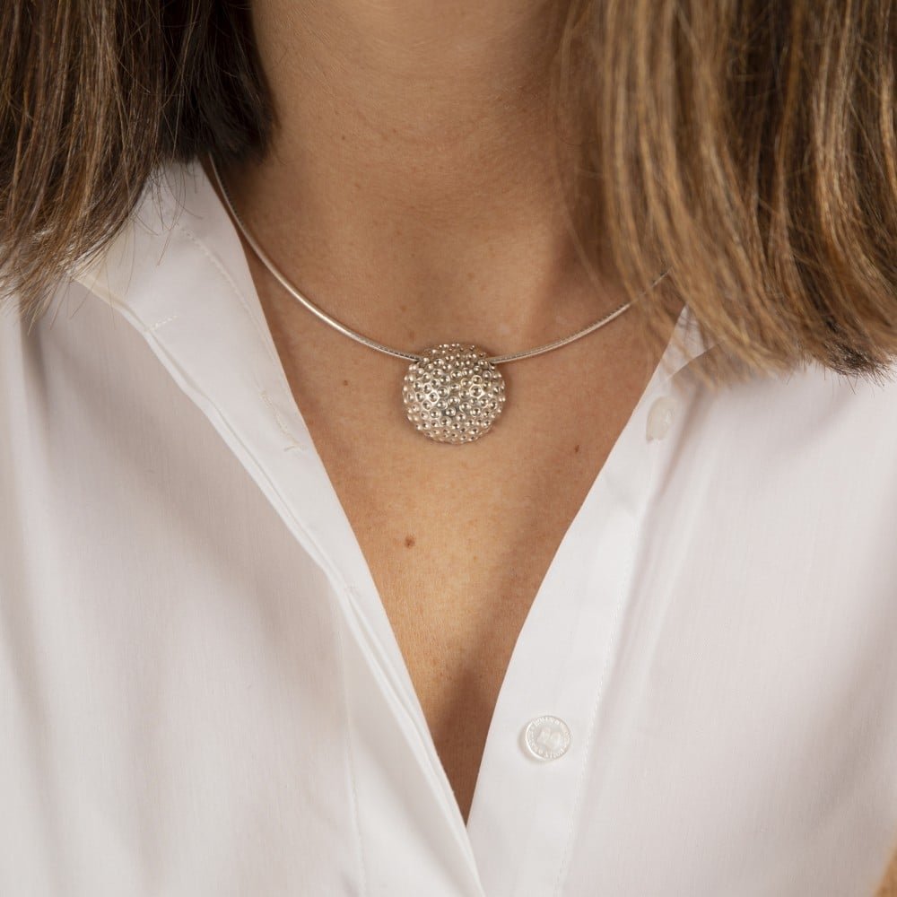 Golf L halsband close up silver circular pendant with bubble texture on a silver chain