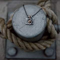 HÅLL OM pendant close up of rough square frame with a circular central cutout and chain loops