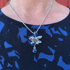 BLÅBÄR halsband med blomformigt silverhänge och blå sten nedhängande från kedja bärs runt halsen
