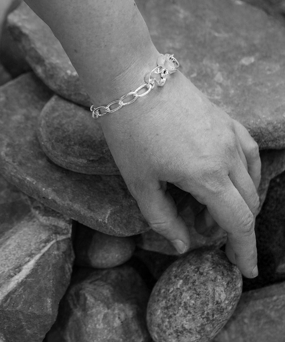 STORMSKÄRS MAJA Nät armband i silver på handleden bland stenar vid stranden