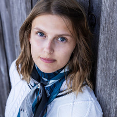 Close up portrait of a woman with blue eyes wearing a blue scarf accessory from the RÅBANDSKNOP scarfring collection