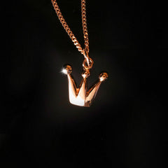 18K rose gold crown pendant on a chain against a dark background