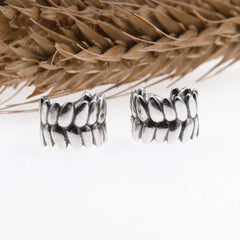Par RÅG stiftörhängen i 925 sterling silver med bladformade segment ligger bredvid varandra framför torkat gräs