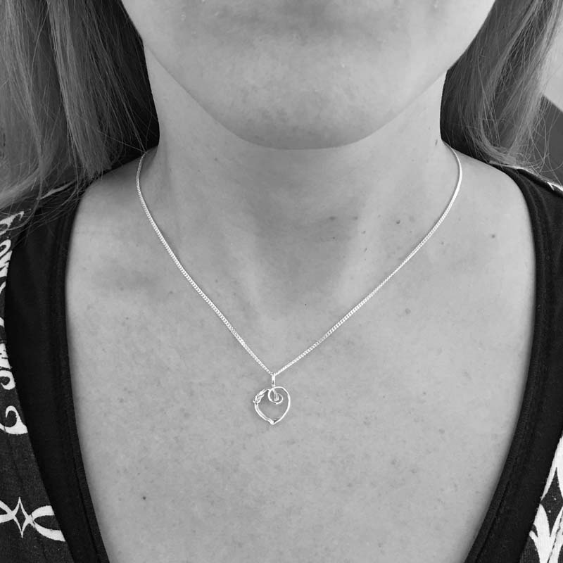 Person wearing a silver heart knot pendant necklace at the collarbone
