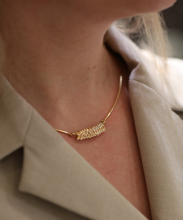 RÅG 18K halsband i gyllene ton med bladformade länkar längs kedjan som följer halsens kontur