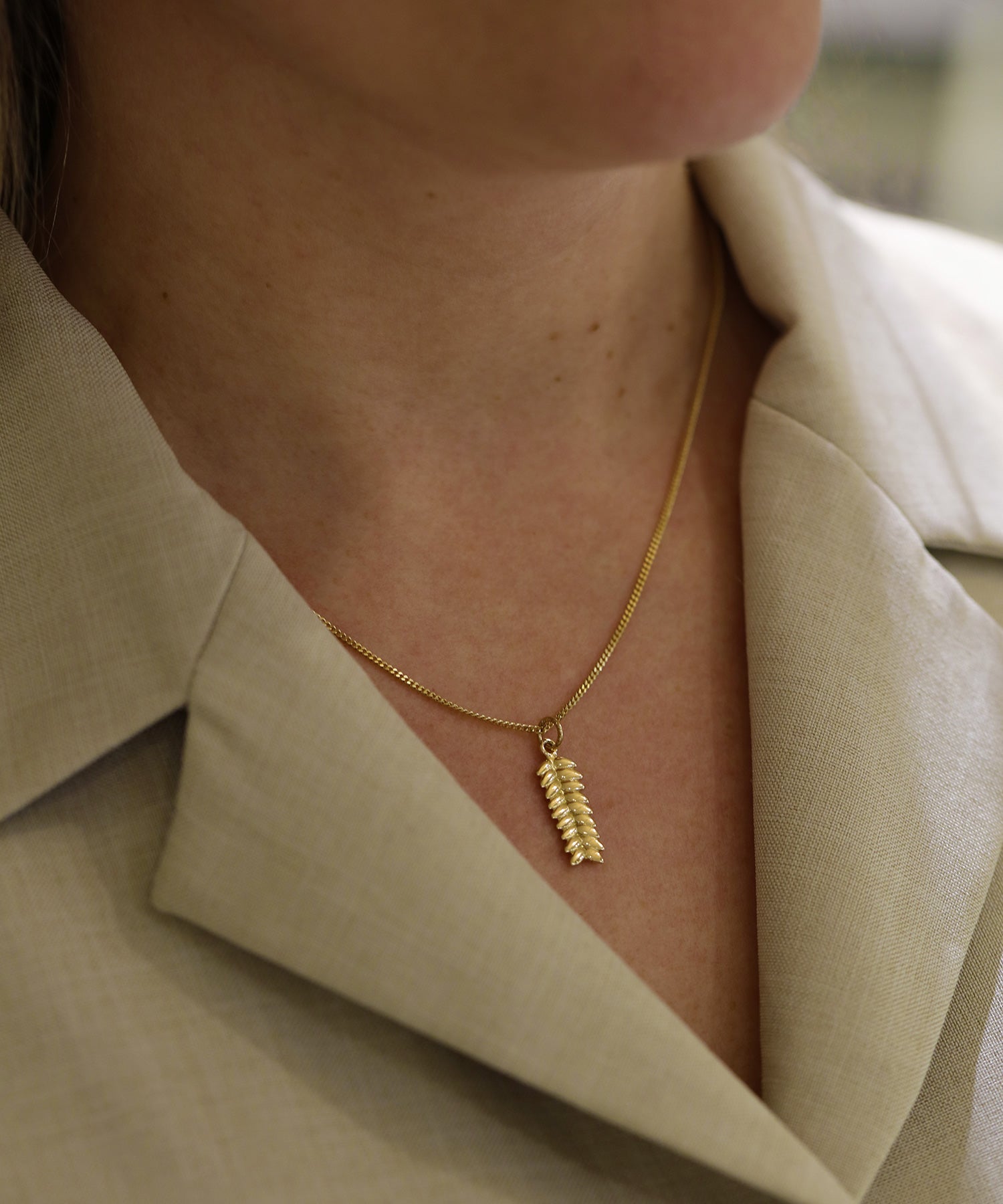 Close-up of the RÅG XS 18K gold leaf pendant necklace resting on the neck above a beige garment
