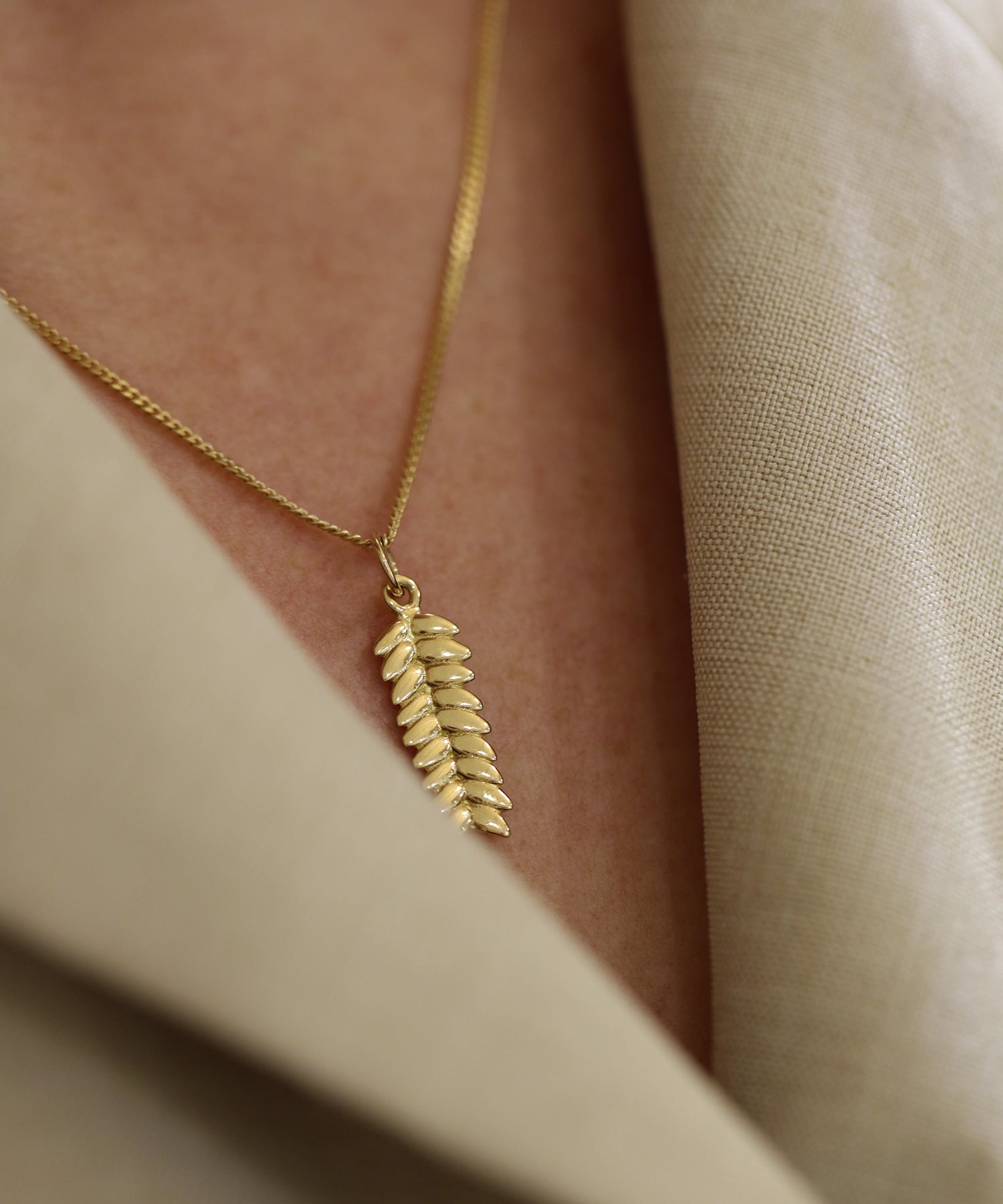 RÅG XS 18K gold leaf pendant necklace worn on a person in a beige blazer