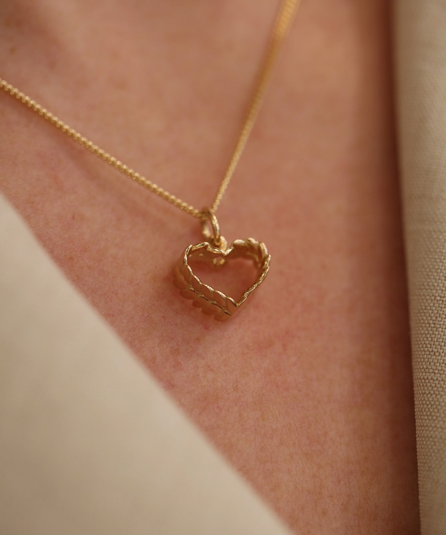 Close up of a twisted gold heart pendant on a delicate chain against skin.