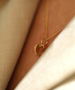 Close up of a gold heart pendant on a thin chain resting against the neck.