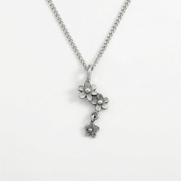Close up of a silver flower pendant necklace on a chain against a white background.