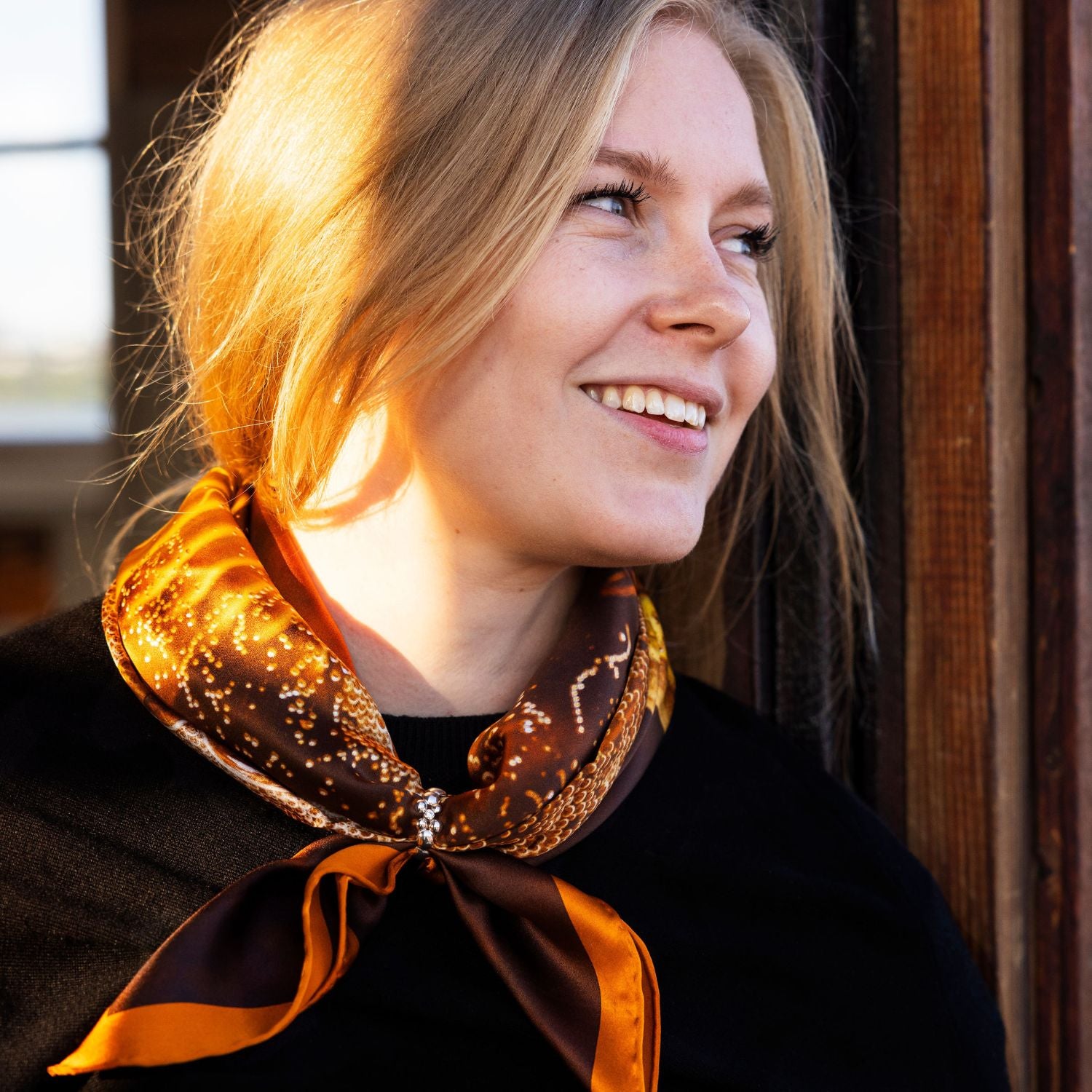 Smiling woman wearing a brown and orange patterned scarf styled with Celebrate Scarfring.