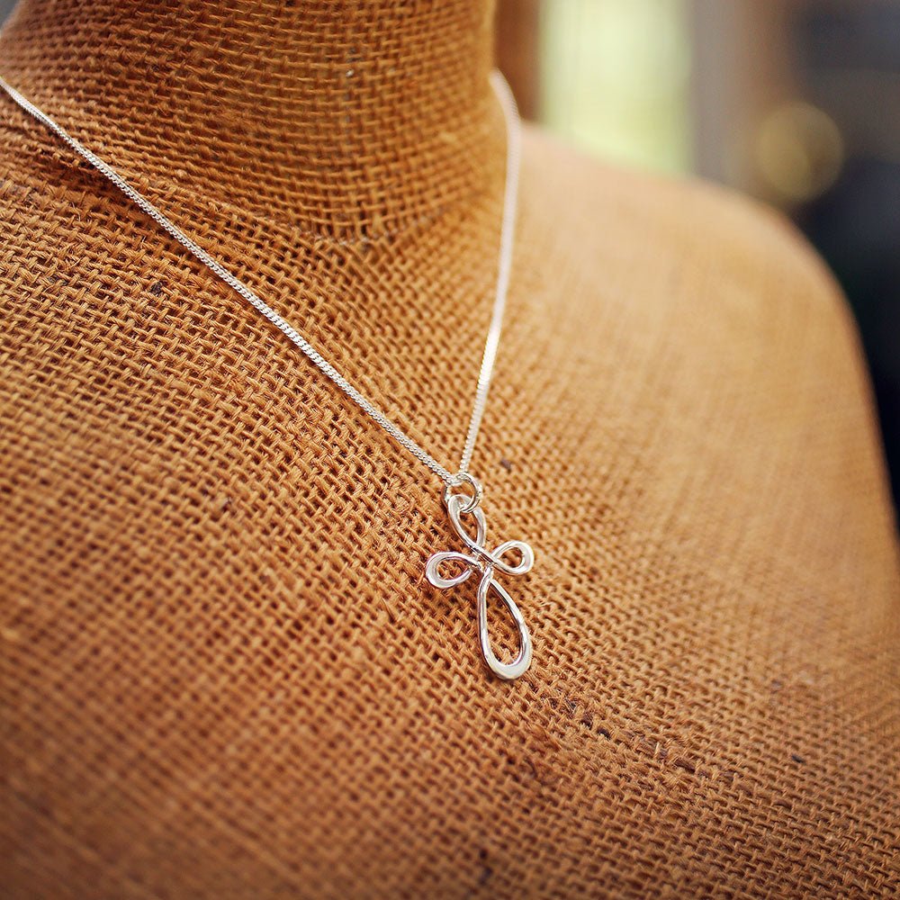 SIRLIGT KORS halsband med handbockat kors i silver på tunn kedja visas på en textilmannequin