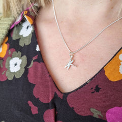 Close up of a silver Trollslända dragonfly pendant resting on a necklace at the neckline.