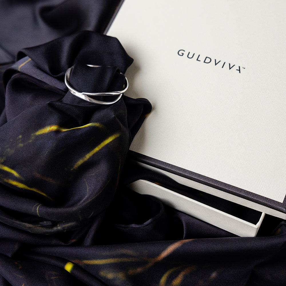 Close up of navy UNDER YTAN scarf with yellow streaks wrapped and secured by a silver ring beside a GULDVIVA box