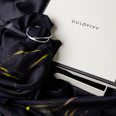 Close up of navy UNDER YTAN scarf with yellow streaks wrapped and secured by a silver ring beside a GULDVIVA box