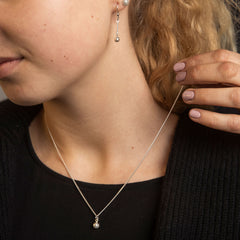 Model wears a silver golf ball pendant necklace and matching drop earrings