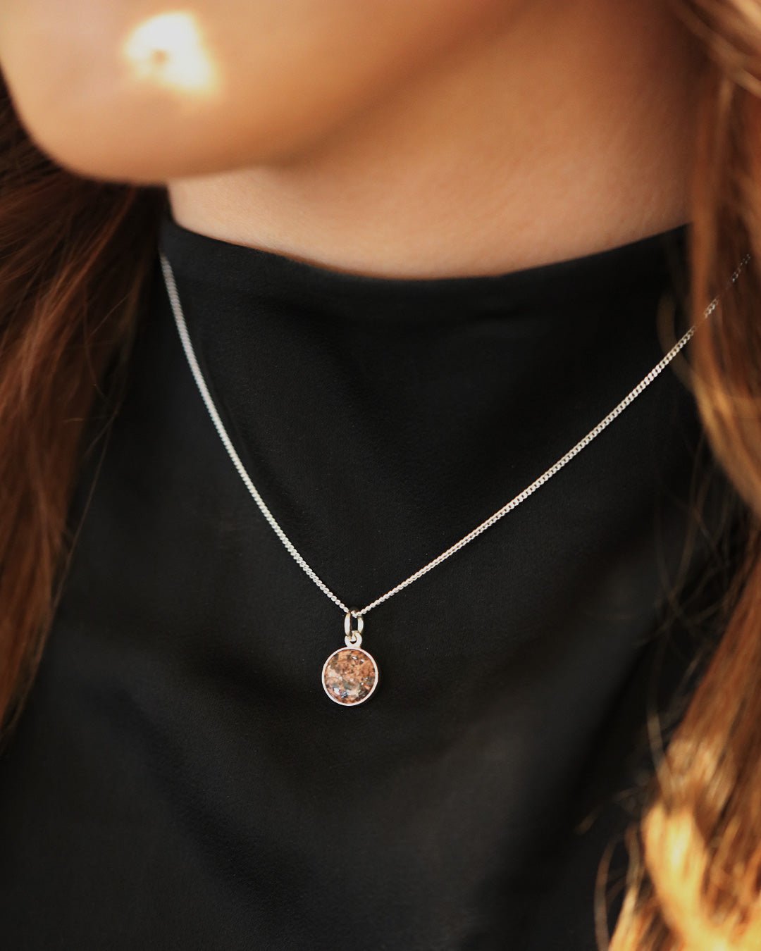 Round red granite pendant set in silver on a slim silver chain worn on a black top.