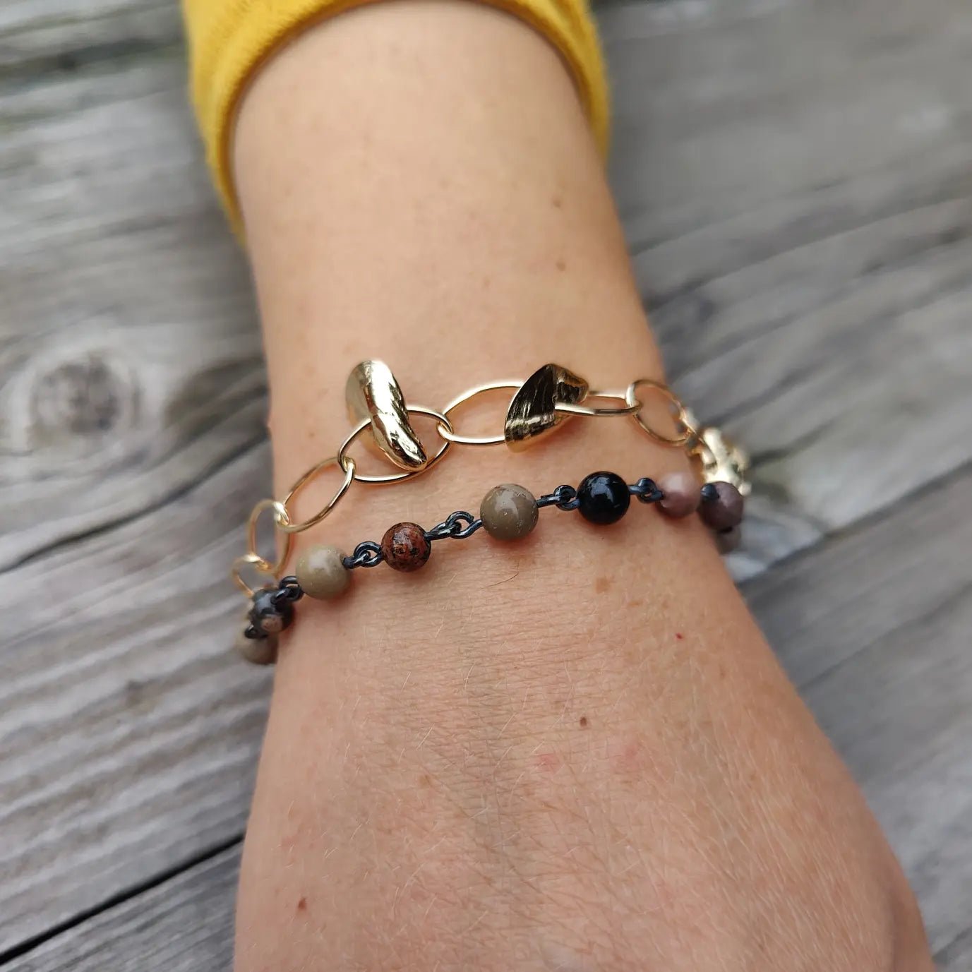 På handleden syns två smycken ett guldigt ringlänk armband och ett pärlarmband i olika färger