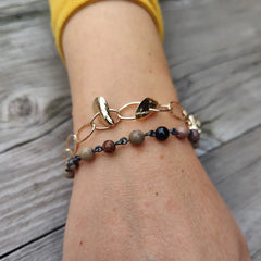 På handleden syns två smycken ett guldigt ringlänk armband och ett pärlarmband i olika färger