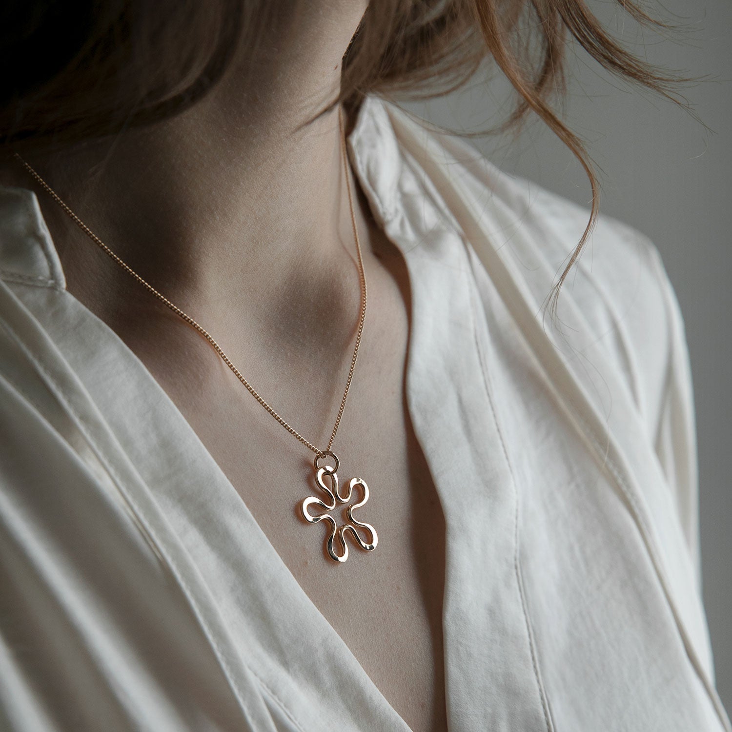 Närbild av BLOMMAN halsband i 18K guld med blomformad hänge mot hud