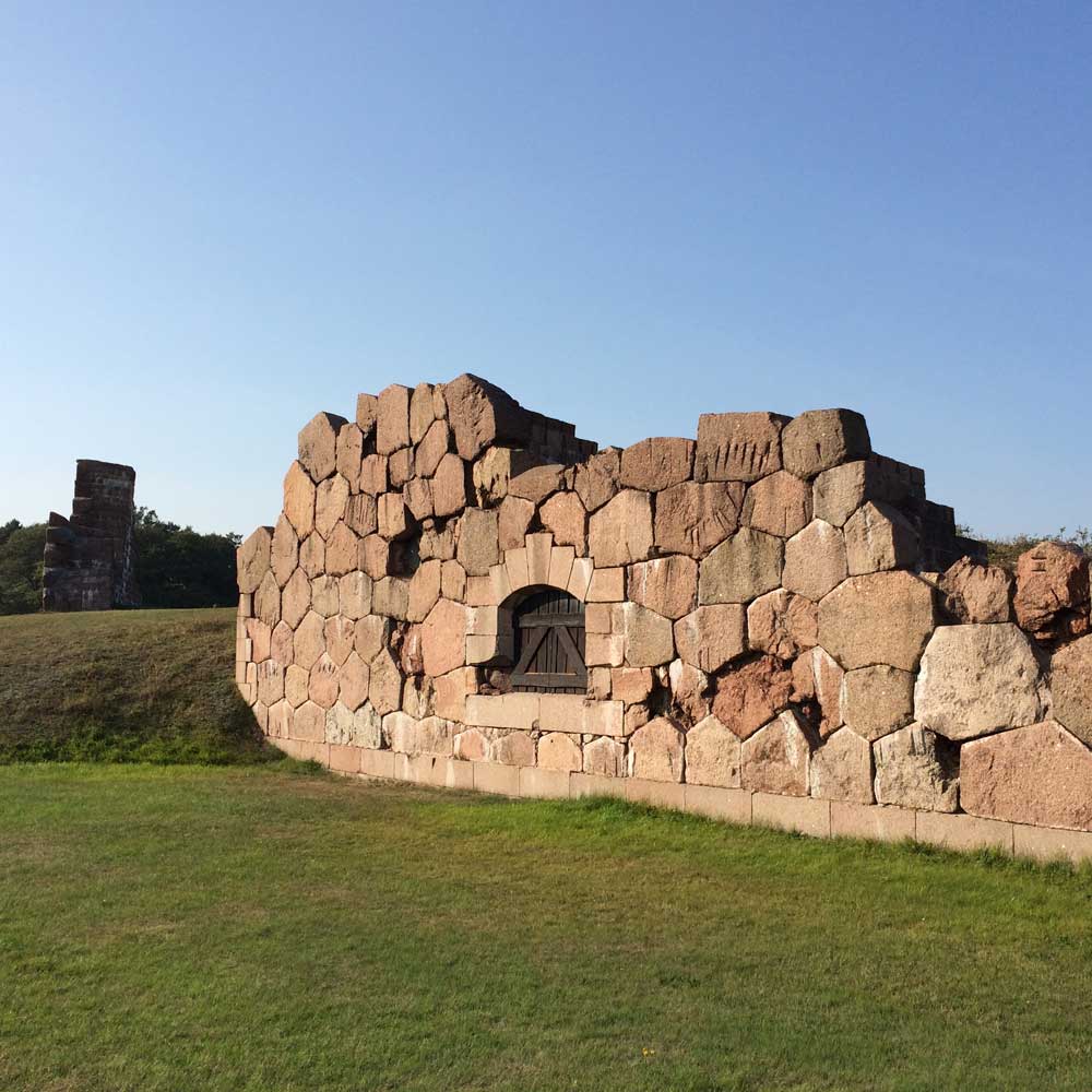 Ruins of Bomarsund fortress built from pink granite blocks with an arched window on a grassy field