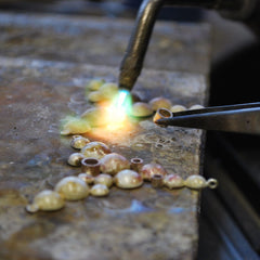 Jewelry making scene with a torch melting beads and champagne colored beads on a workbench