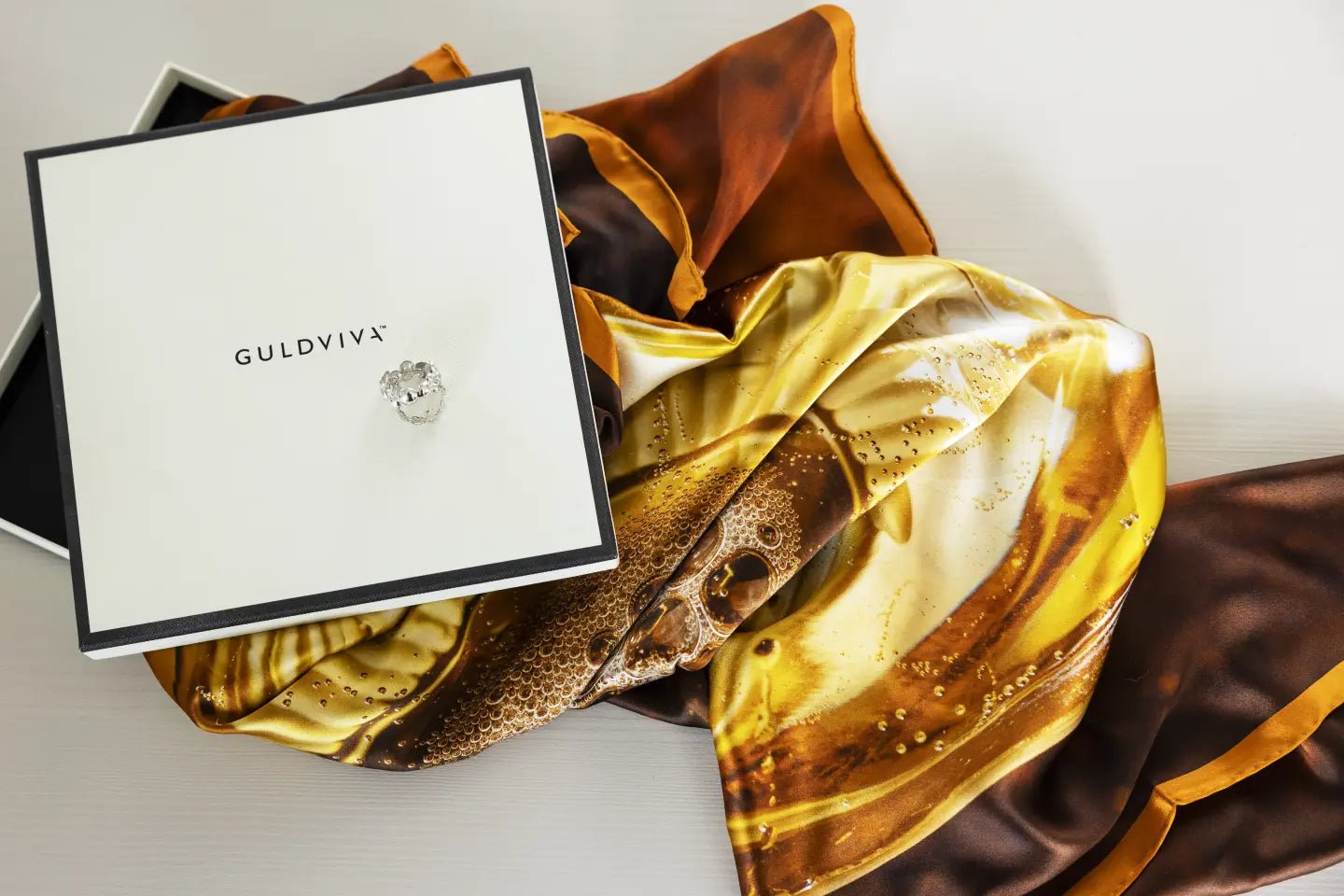Celebrate silk scarf in brown and gold tones displayed in an open gift box.