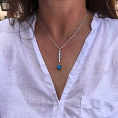 Silvrigt halsband med ett mjukt runt hänge bestående av en vertikal stav, ringar och en blå spektrolit cabochon