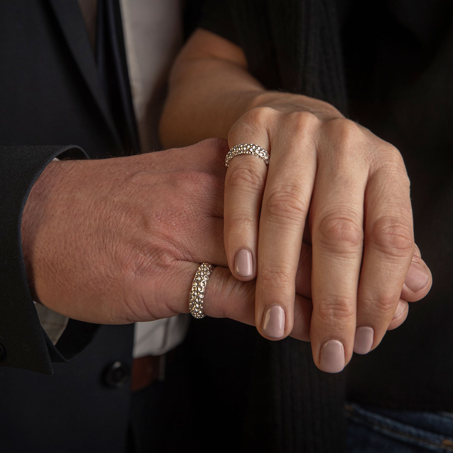 Two hands wearing matching silver rings with a golf ball pattern